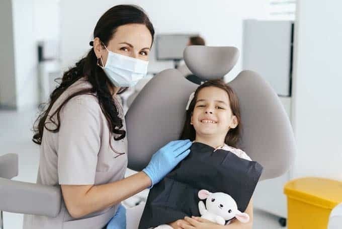 Dental hygienist in mask examining young patient in dental chair at clinic