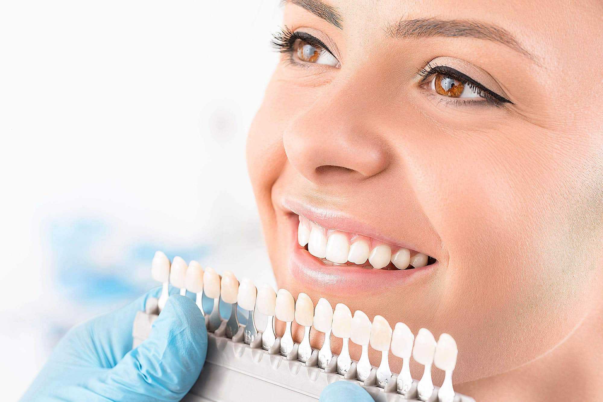 Woman smiling while dentist holds tooth shade guide for color matching during dental consultation.