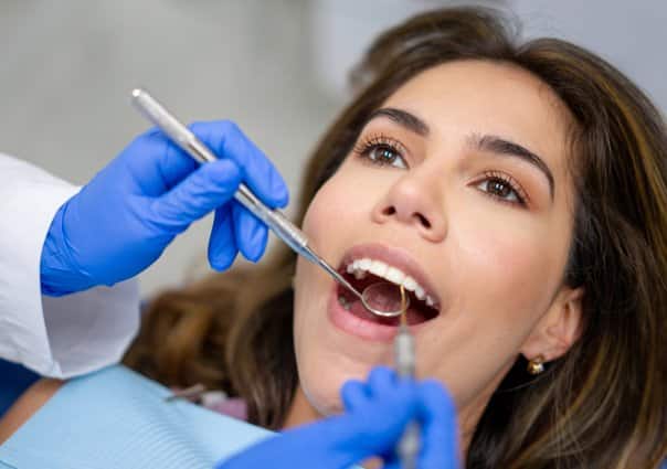 Female patient receiving dental examination from dentist with tools in clinical setting.